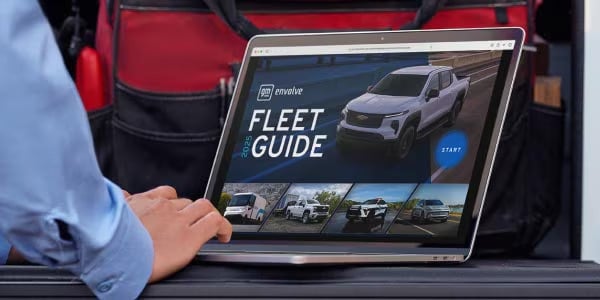 Laptop displaying 2024 Chevy Fleet Guide website with truck images; person touches trackpad.