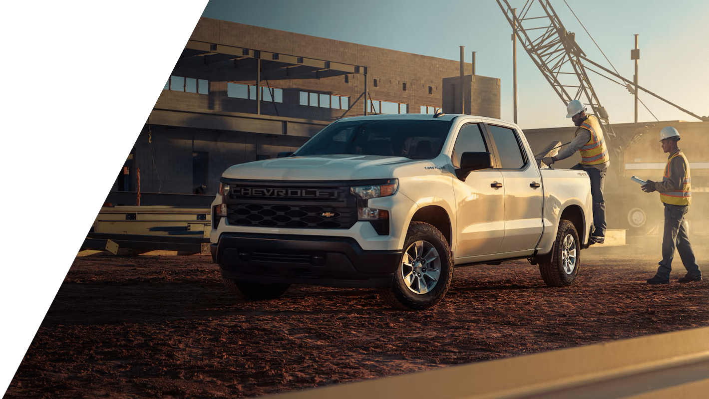 White Chevrolet truck parked at a construction site with two workers nearby, under clear sky.