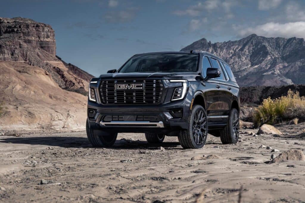 Black GMC SUV on a rocky desert landscape with mountains in the background under a cloudy sky.