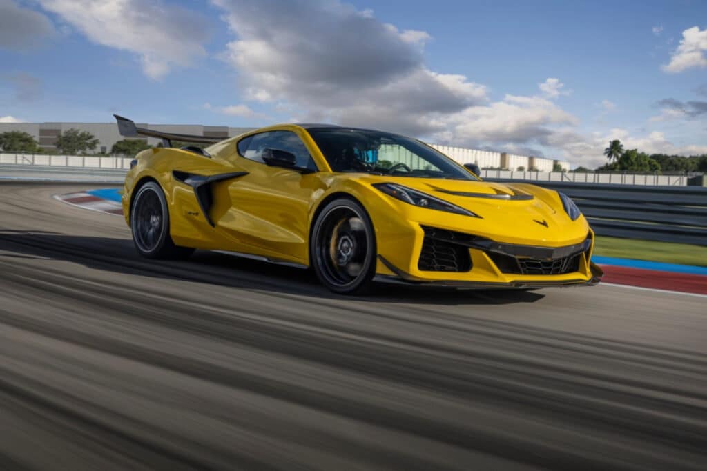 Yellow sports car speeding on a racetrack under a blue sky with fluffy clouds.