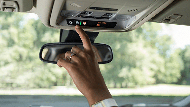 Finger pressing a button on a car's overhead console, with a visible rearview mirror.