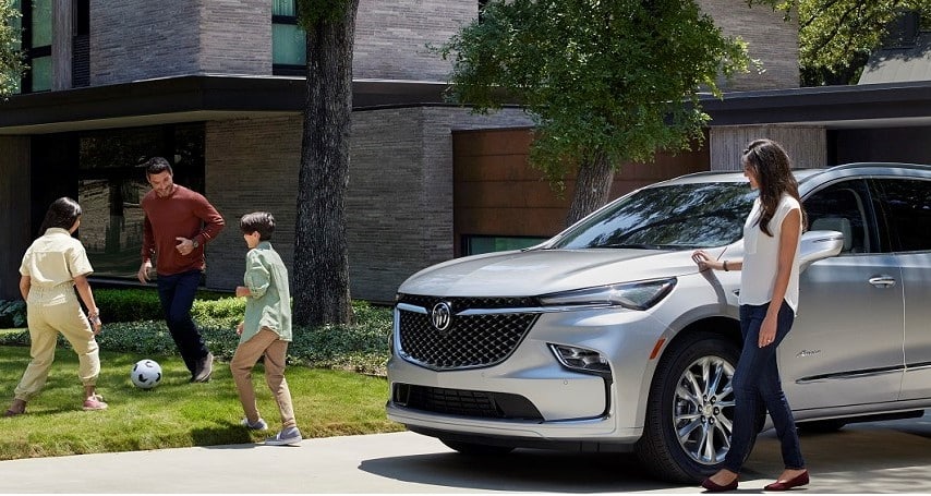A family plays soccer near a silver Buick SUV parked outside a modern house.