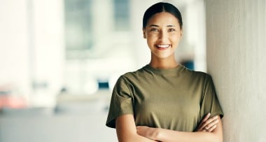 Smiling person in a green shirt standing with arms crossed in a bright indoor space.