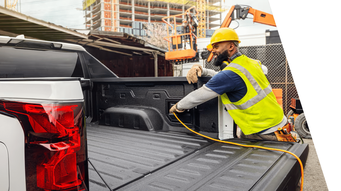 Construction worker in high-visibility vest and hard hat handling cable in truck bed at a construction site.