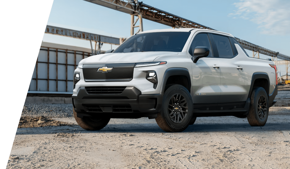 White Chevrolet pickup truck parked on gravel in an industrial area, under a blue sky.