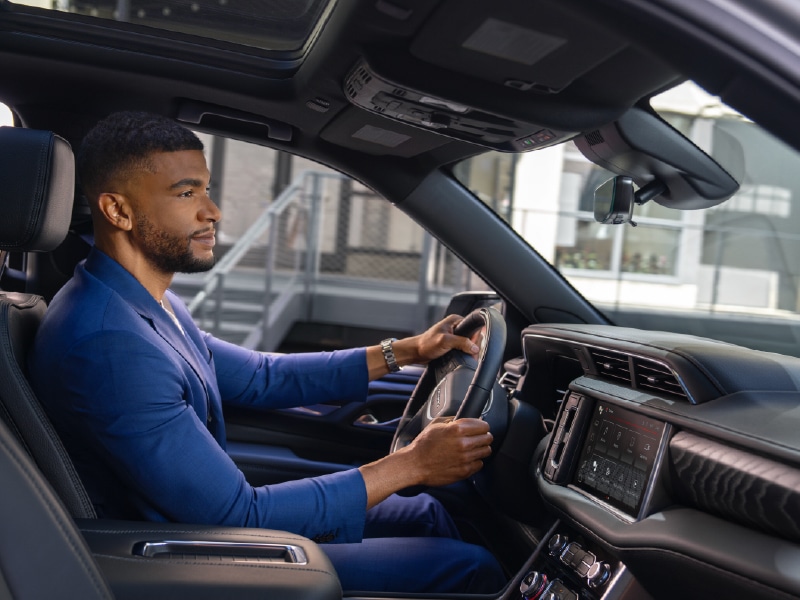Man in a blue suit driving a car, focused on the road, with a modern dashboard visible.