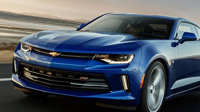 Blue sports car driving on a coastal road at sunset, showcasing aerodynamic design and sleek lines.