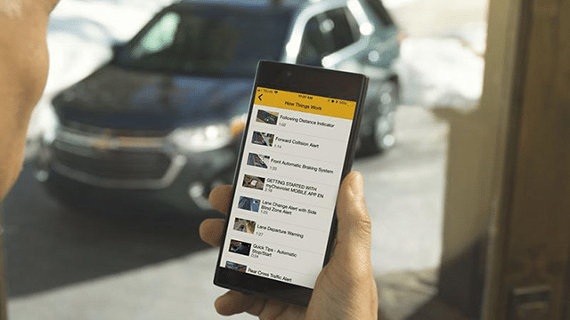 Person holding a smartphone displaying a driving assistance app, with a parked SUV in the background.