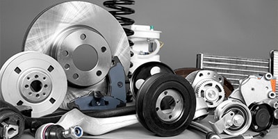 Various automotive parts, including brake discs, shock absorbers, and gears, are arranged on a grey background.