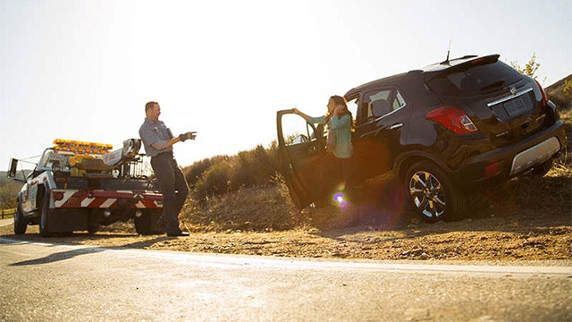 Tow truck driver assists a woman with a black SUV stuck on a rural roadside.