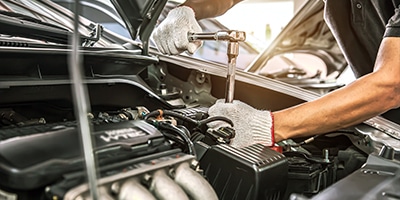 Mechanic using a wrench to repair a car engine, highlighting automotive maintenance.