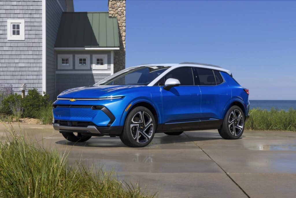 Blue electric SUV parked by a coastal house, featuring modern design and sleek lines.