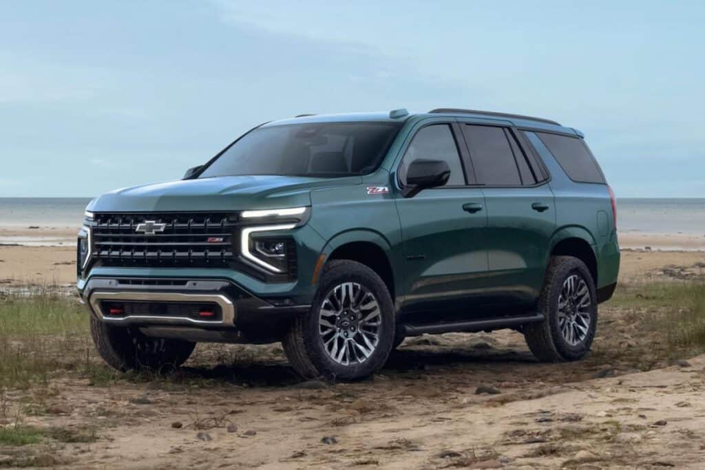 Green SUV parked on a sandy beach with the ocean in the background, under a clear sky.