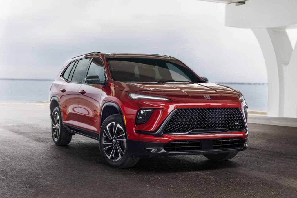 Red SUV parked by the water, showcasing a bold grille design and modern styling.