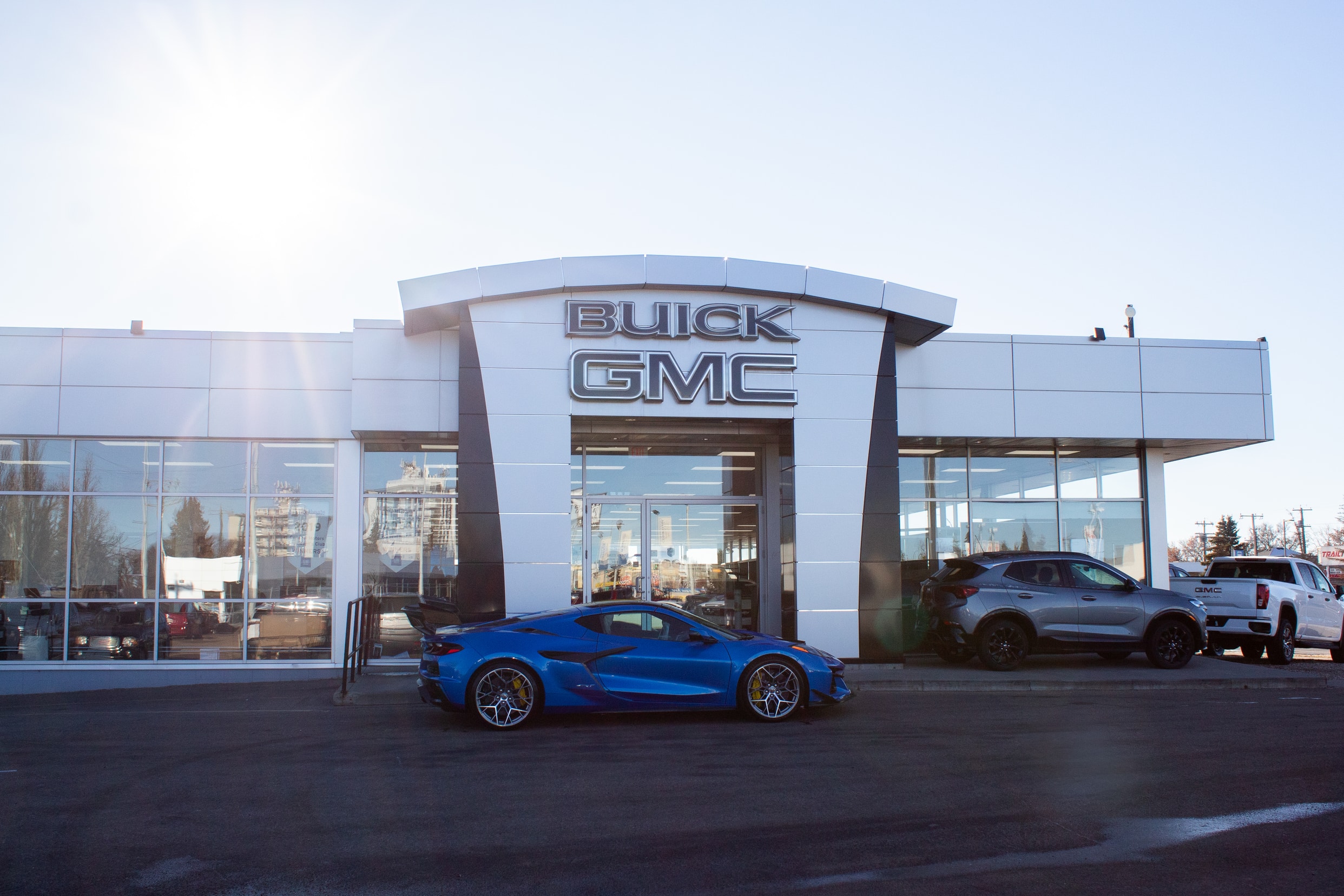 Buick GMC dealership exterior with a blue sports car parked in front under a sunny sky.